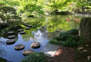 a beautiful green park with a lake with stepping stones.