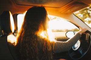 woman with long hair driving a car with the sunlight coming in behind her. 