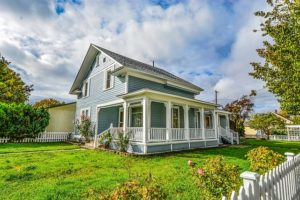 older style two story home with a front porch surrounded by a picket fence.