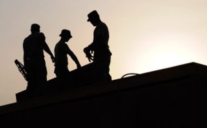 dark silhouettes of three male construction workers standing on a roof as the sun goes down.