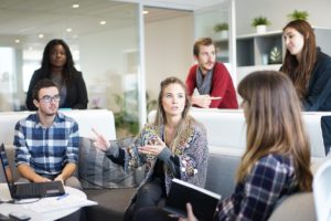 Group of millennials sitting in an office-setting discussing business over computer.