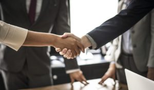 Two professionals shaking hands in front of a group of other professionals.