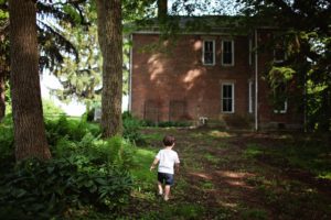 A little kid outside of a brick house.