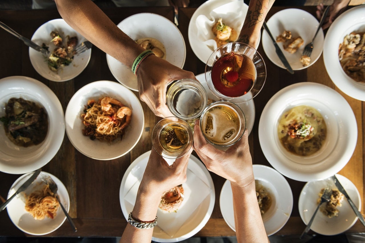 A large group of people enjoying several plates of food and wine.