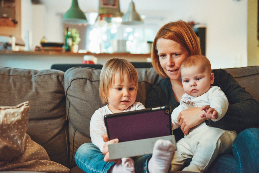 Woman and two children using a tablet on a couch.