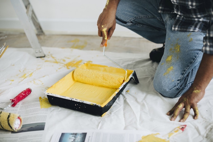 A person rolling a paint roller in yellow paint.