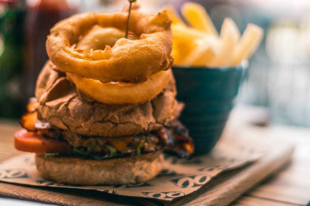 A burger topped with onion rings and a side of fries.